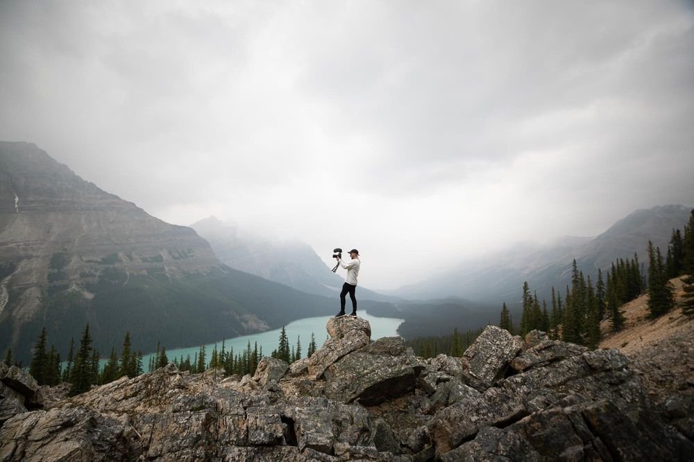 Seorang pria dengan kamera dan gunung sebagai latar belakangnya