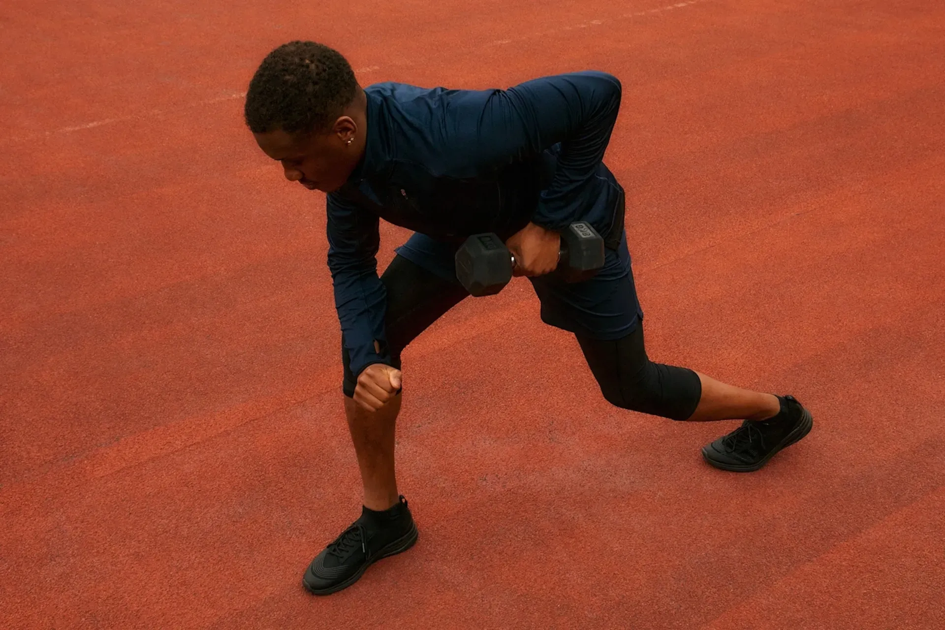 An athlete warming up with weights on a running track
